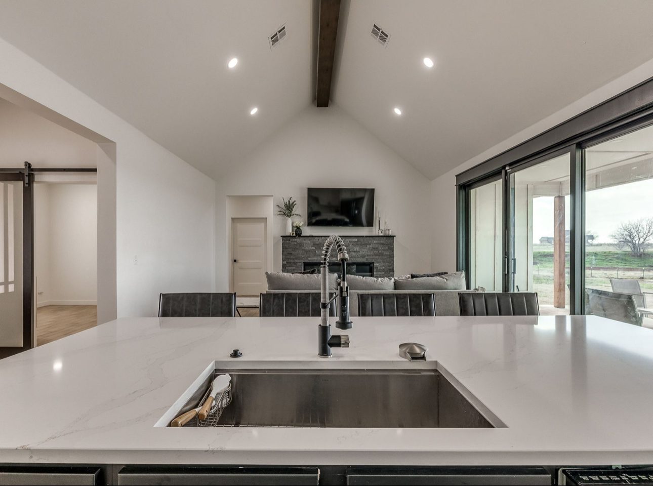 A white quartz island with an undermount sink and matte black faucet, looking across to a stone fireplace and sliding doors