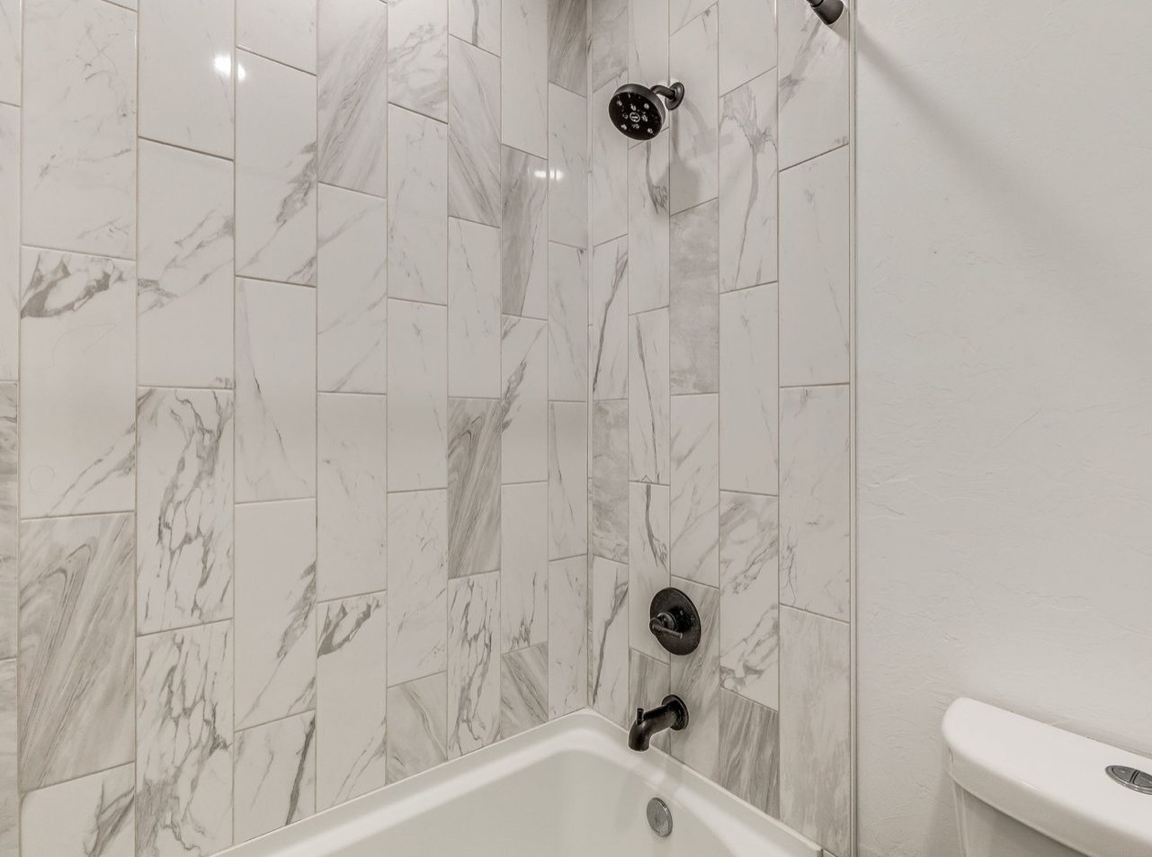 A tub and shower surround in tall white marble look tile with matte black fixtures