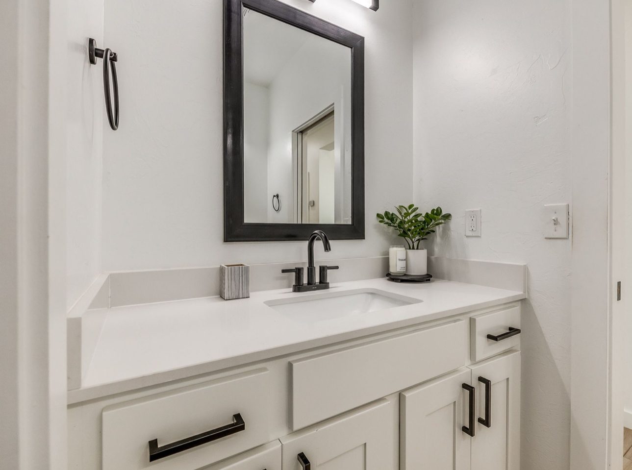 A white shaker vanity with a quartz top, matte black faucet and pulls, and a black framed mirror above