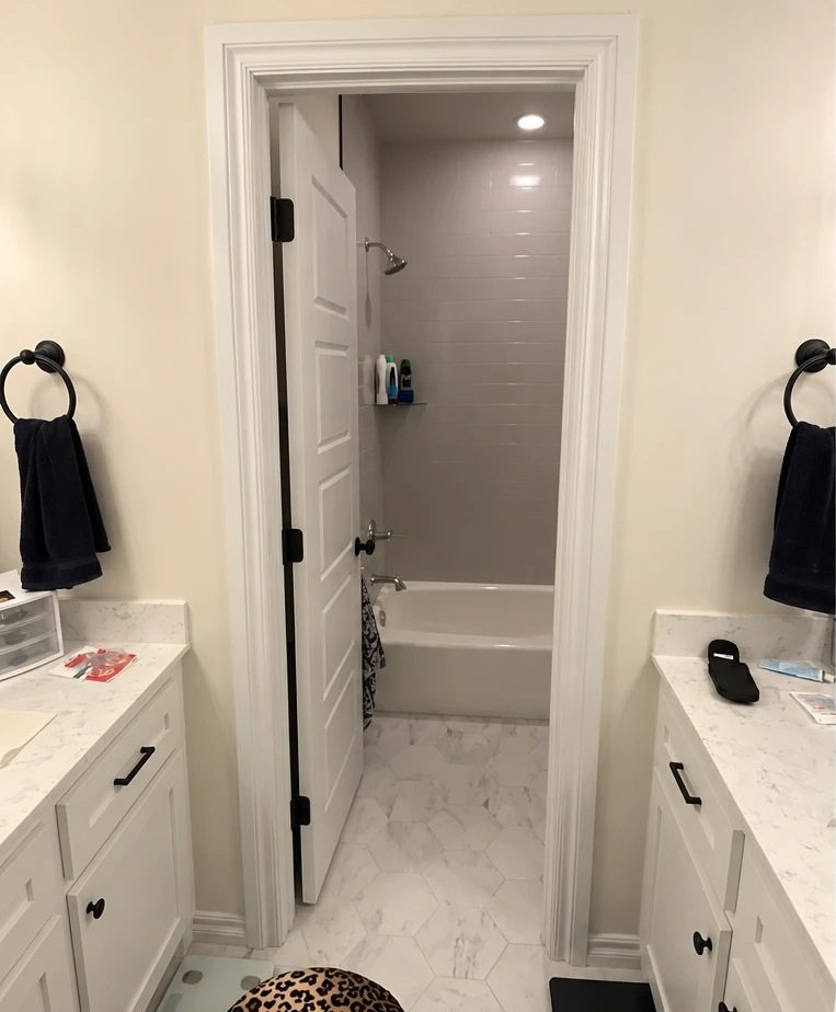 The bathroom before the work: an alcove tub behind a panel door, with a grey tiled surround and a shower head over the tub