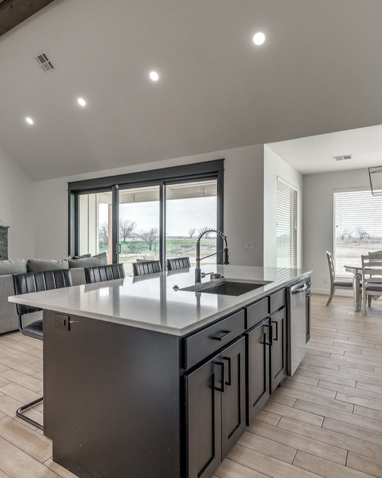 A kitchen with a dark island and white quartz top, stainless appliances, and a stone fireplace in the living room beyond