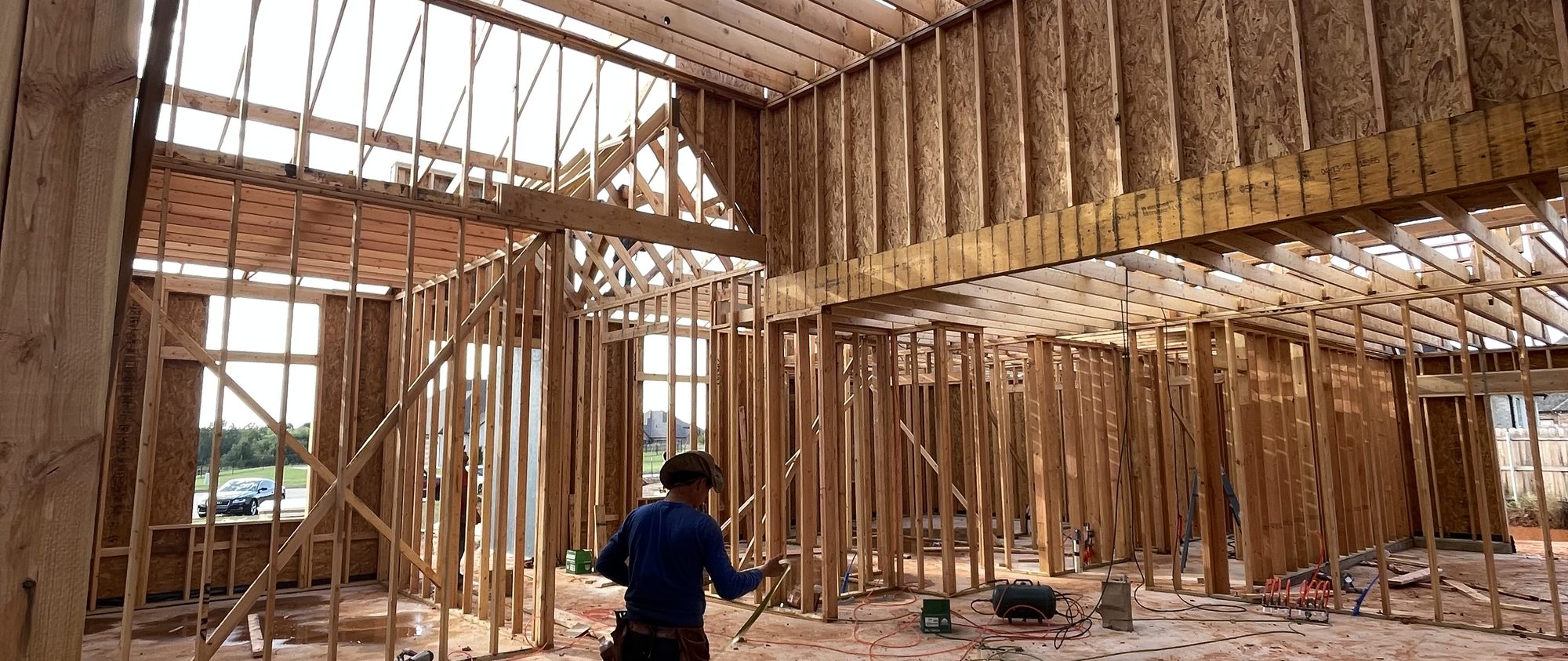 The great room of the Honeybee house under framing, with the vaulted ceiling framed out, daylight coming through the window openings, and a carpenter working on the floor
