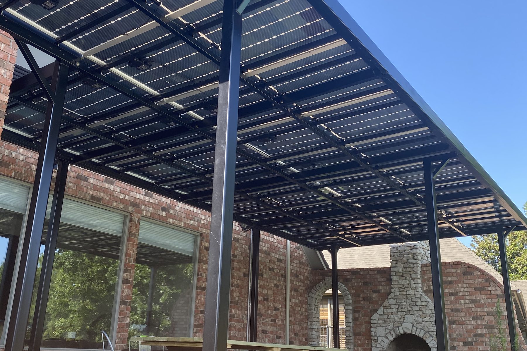 The steel pergola frame carried on brick columns, seen from underneath with the outdoor fireplace and the terrace beyond
