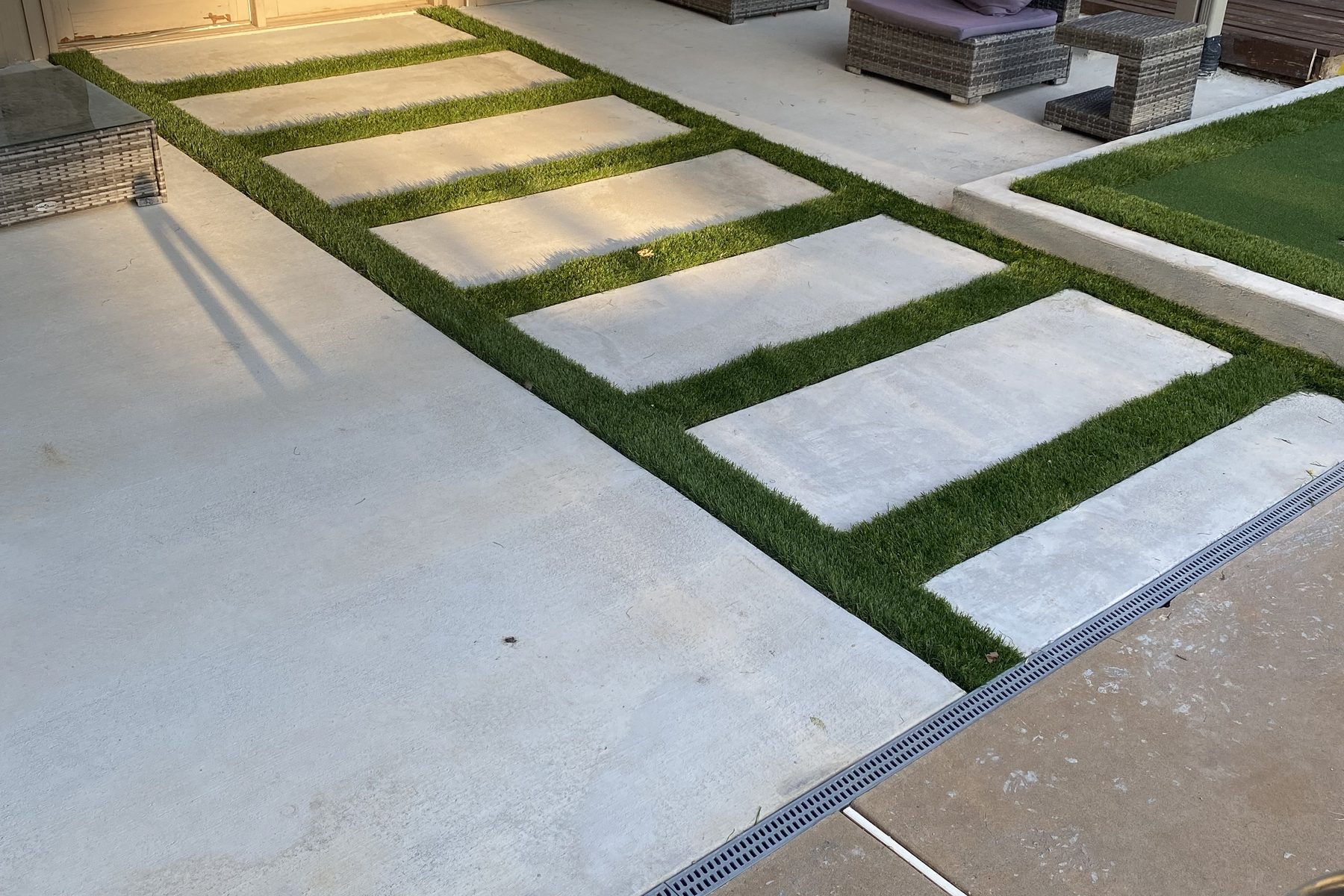 Poured concrete bands with synthetic turf inlaid in the joints between them, running past the covered patio to a channel drain