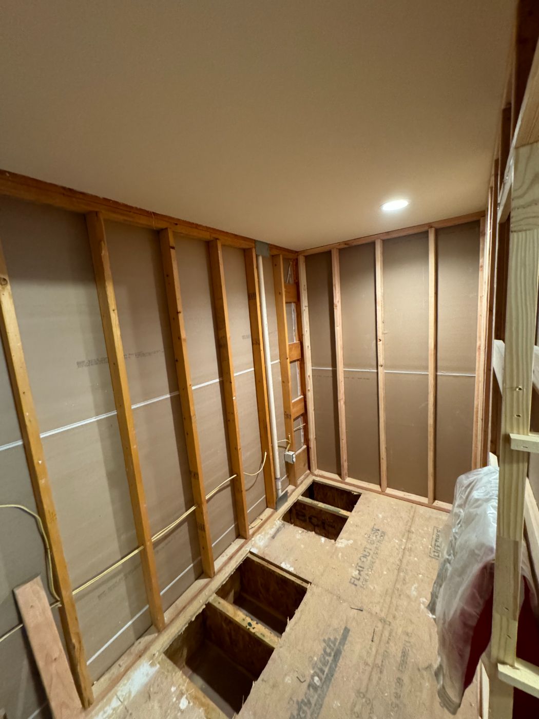 New framing along a narrow room under construction, with the subfloor opened for plumbing
