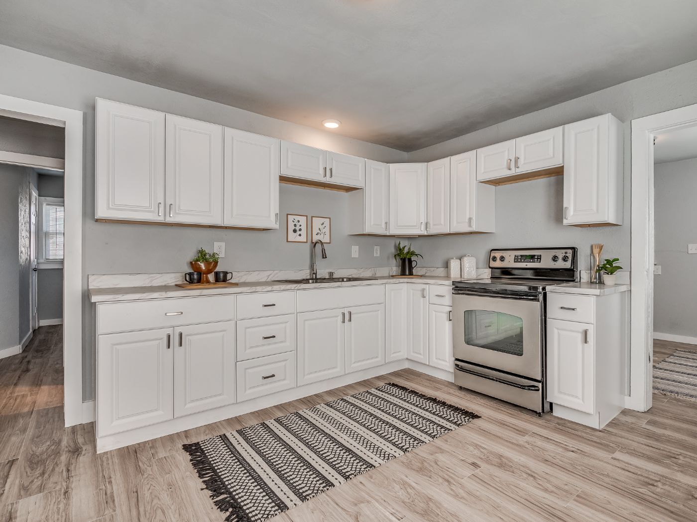 A remodeled kitchen with white raised panel cabinets, a stainless range and new wood look flooring