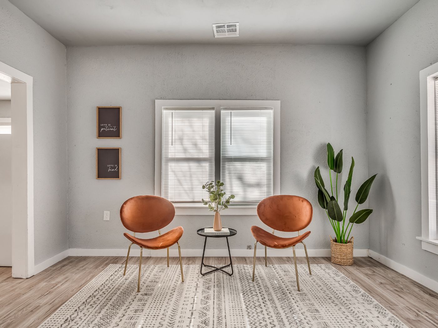 A finished living room with new flooring, a patterned rug and two rust colored chairs by the window